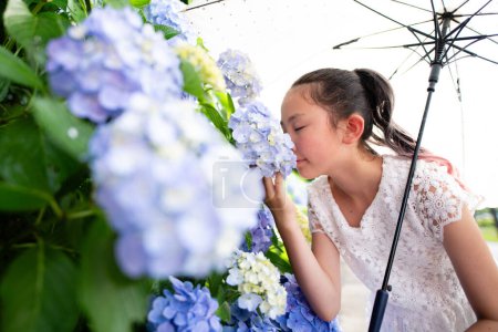 Téléchargez les photos : Asiatique fille avec parapluie odeur fleurs dans parc - en image libre de droit