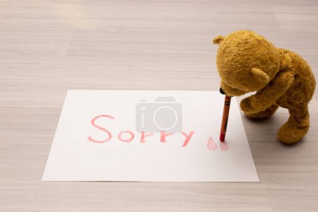 Téléchargez les photos : Ours en peluche écrivant "désolé" sur papier - en image libre de droit