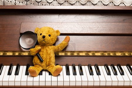 Téléchargez les photos : Un ours en peluche avec une loupe assise sur un clavier de piano - en image libre de droit