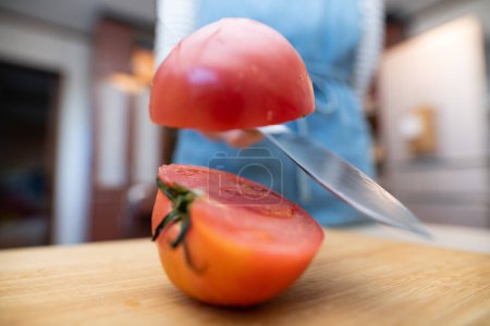 Foto de Una mujer en un delantal cortando un tomate - Imagen libre de derechos