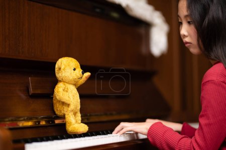 Photo for Teddy bear teaching piano to girl - Royalty Free Image