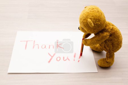 Téléchargez les photos : Ours en peluche écrivant "merci" avec un crayon sur papier - en image libre de droit