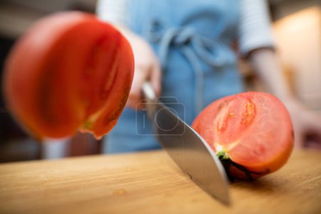 Foto de Una mujer en un delantal cortando un tomate - Imagen libre de derechos