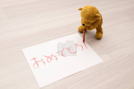Téléchargez les photos : Ours en peluche écrivant félicitations en japonais avec des crayons sur papier - en image libre de droit