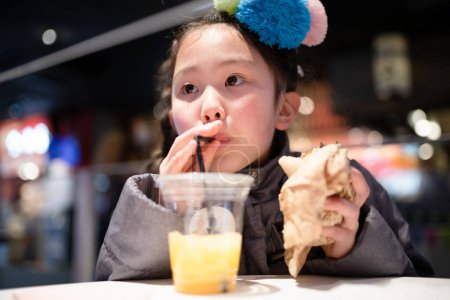 Téléchargez les photos : Fille manger de la restauration rapide dans le magasin - en image libre de droit