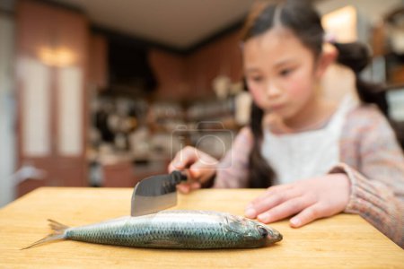 Photo for Girl cooking sardine with a kitchen knife - Royalty Free Image