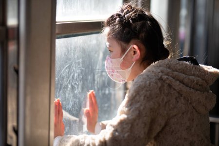 Foto de Una chica con una máscara y mirando por la ventana - Imagen libre de derechos