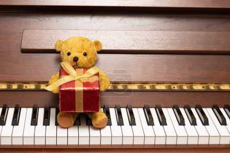 Photo for Teddy bear with a present sitting at the piano - Royalty Free Image