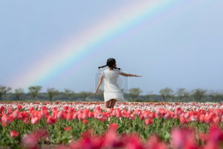 Foto de Una chica jugando en un jardín de flores con un arco iris - Imagen libre de derechos