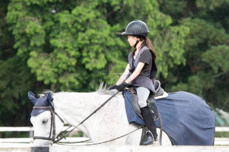Téléchargez les photos : Fille pratiquant l'équitation un jour de pluie - en image libre de droit