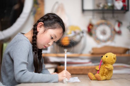 Téléchargez les photos : Un enfant étudie à la maison et un ours en peluche veille sur - en image libre de droit