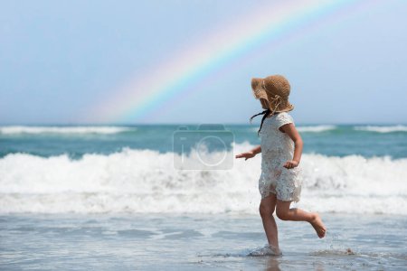 Téléchargez les photos : Petite fille jouant sur la plage avec un arc-en-ciel - en image libre de droit