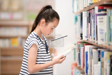 Téléchargez les photos : Fille choisissant des livres dans la bibliothèque - en image libre de droit