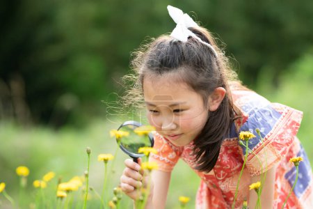 Téléchargez les photos : Fille observant des fleurs avec loupe - en image libre de droit