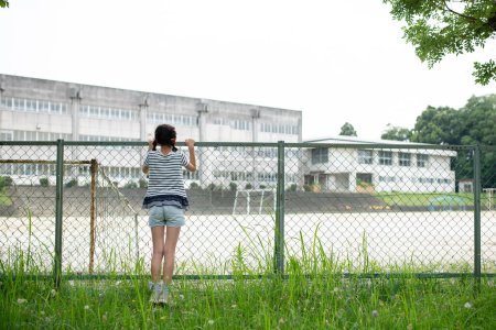 Téléchargez les photos : Enfant regardant l'école de l'extérieur de la clôture - en image libre de droit