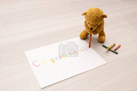 Foto de Osito de peluche escribiendo 'felicitaciones' en papel con lápices de colores - Imagen libre de derechos
