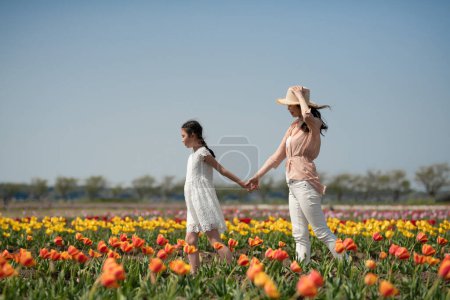 Foto de Madre e hija cogidas de la mano en el jardín de flores - Imagen libre de derechos
