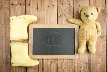 Photo for Rain boots and blackboard and teddy bear on wooden background - Royalty Free Image