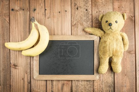 Foto de Plátanos y pizarra y osito de peluche sobre fondo de madera - Imagen libre de derechos