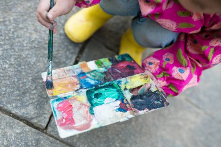 Téléchargez les photos : Petite fille peignant un tableau avec un pinceau dans la rue - en image libre de droit