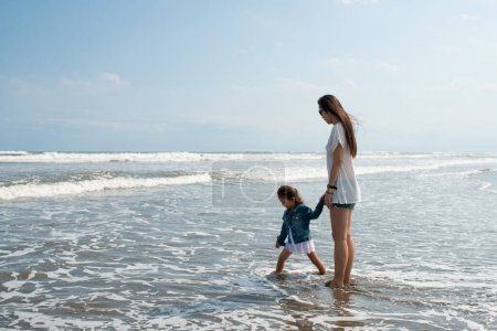 Téléchargez les photos : Mère et fille jouant main dans la main sur la plage - en image libre de droit