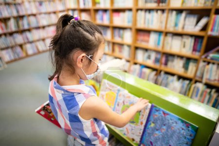 Photo for Girl wearing a mask choosing a book in the library - Royalty Free Image