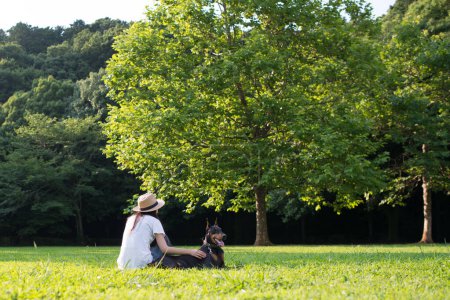 Téléchargez les photos : Femme se détendre sur la pelouse avec le Doberman - en image libre de droit