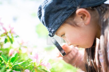 Téléchargez les photos : Belle petite fille asiatique à la recherche de fleurs avec loupe - en image libre de droit
