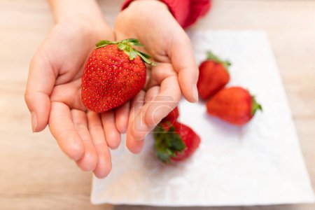 Téléchargez les photos : Enfant tient fraise fraîche dans les mains - en image libre de droit