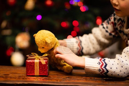 Téléchargez les photos : Les mains des enfants jouent avec le cadeau de Noël et l'ours en peluche - en image libre de droit