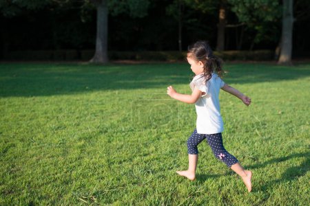 Téléchargez les photos : Asiatique petite fille courir sur herbe dans l 'parc - en image libre de droit