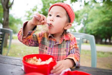 Téléchargez les photos : Petite fille manger le déjeuner à l'extérieur - en image libre de droit