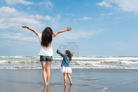 Téléchargez les photos : Mère et fille étendant leurs mains sur la plage - en image libre de droit