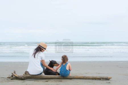 Téléchargez les photos : Mère et fille et un chien assis sur la plage - en image libre de droit