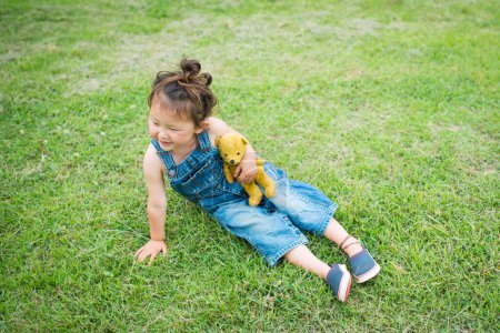 Photo for Girl playing with teddy bear wearing overalls - Royalty Free Image