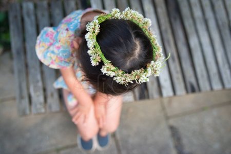 Téléchargez les photos : Fille assise sur un banc et portant une couronne de fleurs - en image libre de droit