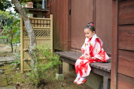 Téléchargez les photos : Asiatique petite fille dans traditionnel japonais kimono sur banc - en image libre de droit
