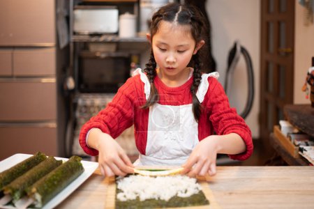 Foto de Una chica en un delantal haciendo rollos de sushi - Imagen libre de derechos