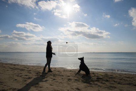 Foto de Mujer que juega con Doberman en la playa - Imagen libre de derechos