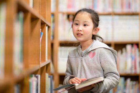 Téléchargez les photos : Petite fille choisissant un livre à la bibliothèque - en image libre de droit