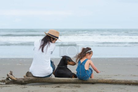 Foto de Madre e hija y un perro sentado en la playa - Imagen libre de derechos
