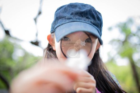 Téléchargez les photos : Un enfant observant une fleur blanche avec une loupe - en image libre de droit