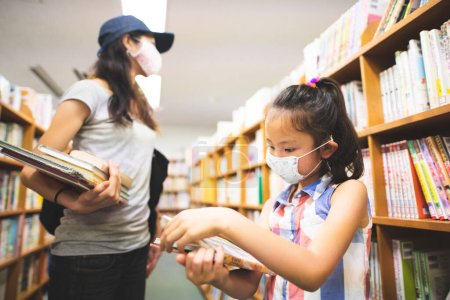 Mother and daughter wearing masks choosing books at the library