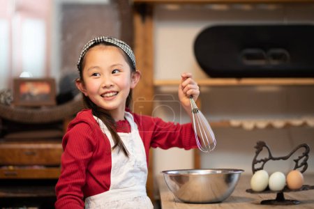 Photo for Smiling asian little girl in apron cooking  in kitchen - Royalty Free Image
