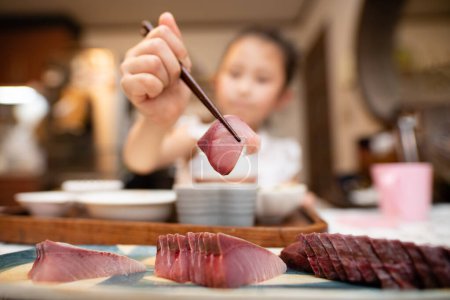Téléchargez les photos : Un enfant qui prend du sashimi avec des baguettes - en image libre de droit