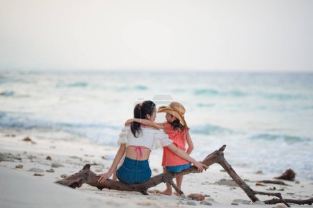 Foto de Madre e hija sentadas en madera a la deriva en la playa - Imagen libre de derechos