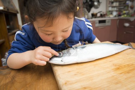 Téléchargez les photos : Mignonne petite fille asiatique avec du poisson frais dans la cuisine - en image libre de droit