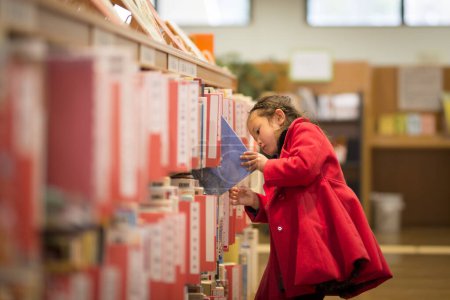 Foto de Joven asiático chica en rojo vestido elegir libro en biblioteca - Imagen libre de derechos
