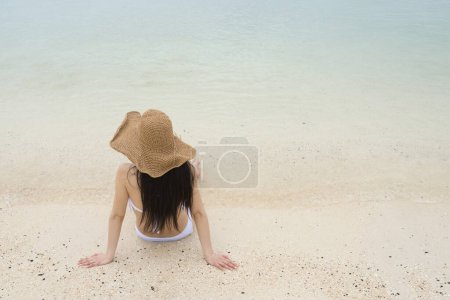 Téléchargez les photos : Femme en maillot de bain assis sur la plage - en image libre de droit