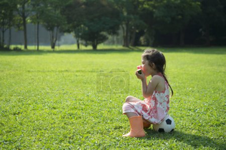Photo for Girl eating watermelon sitting on ball on lawn - Royalty Free Image